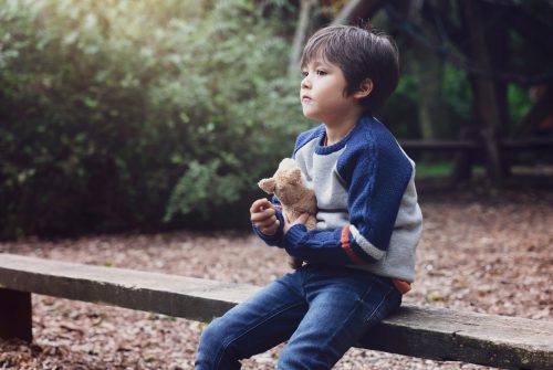 Emotional portrait of Lonely kid hugging dog toy sitting alone in the playground, Sad child sitting with his toy with looking deep in through, little boy playing alone with  thinking face.